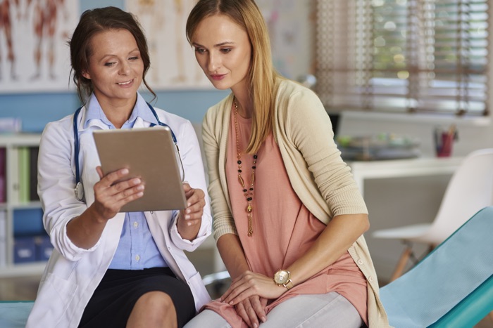 A doctor and a patient sitting together in a medical office, looking at a tablet and discussing health information.